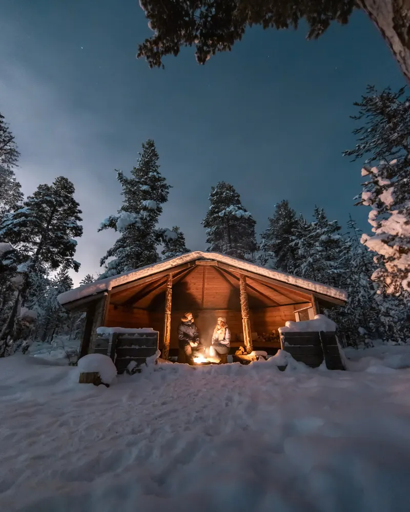 Guests by a campfire in a lean-to shelter at night